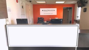 A reception desk at Magnison Hotel with a sign above it, a computer, and a telephone. - Magnuson Hotel Baton Rouge East (Baton Rouge)