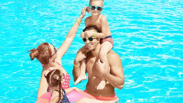 A family in a swimming pool with a child on an adult's shoulders. - Magnuson Hotel Baton Rouge East (Baton Rouge)
