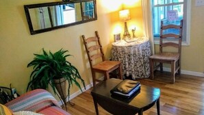Una sala de estar acogedora con un sofá, una mesa de centro, una silla, una mesita de noche con lámpara y una planta en maceta.