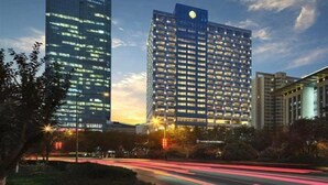 A modern high-rise building with a prominent logo on the top, surrounded by other buildings and a well-lit street. - Intercontinental Xi an North (Xi'an)