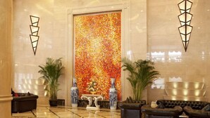 A lobby with a large colorful mosaic wall, two potted plants, a reception desk, and black leather sofas. - Friend Hotel Shanghai (Shanghai)
