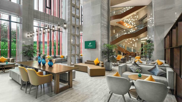 A spacious lobby with a central seating area, a staircase, and a large screen displaying the hotel's name. - Holiday Inn Chengdu Airport (Chengdu)