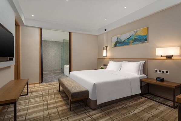 A hotel room with a bed, bedside table, bench, and a TV.
