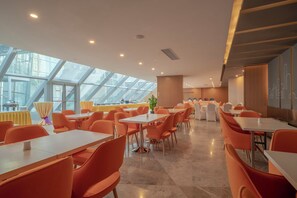 A modern dining area with high ceilings and skylights, featuring orange chairs and white tables. - Holiday INN Express Qingdao Innovation Park (Qingdao)