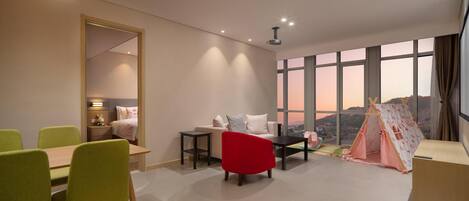 A modern living room with a dining area, a red chair, a sofa, a small table, and a tent-like play structure.