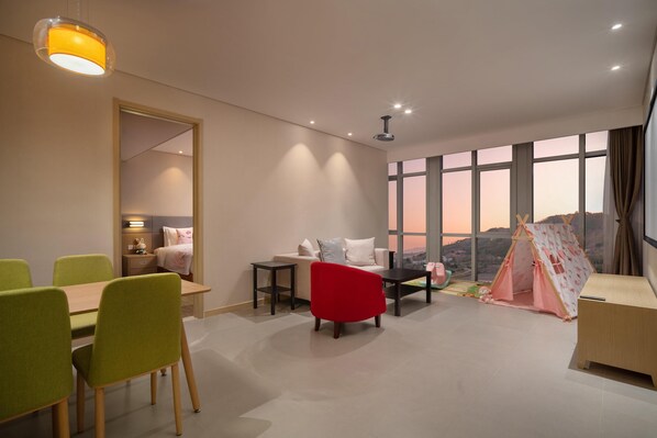 A modern living room with a dining area, a red chair, a sofa, a small table, and a tent-like play structure. - Holiday INN Express Qingdao Innovation Park (Qingdao)