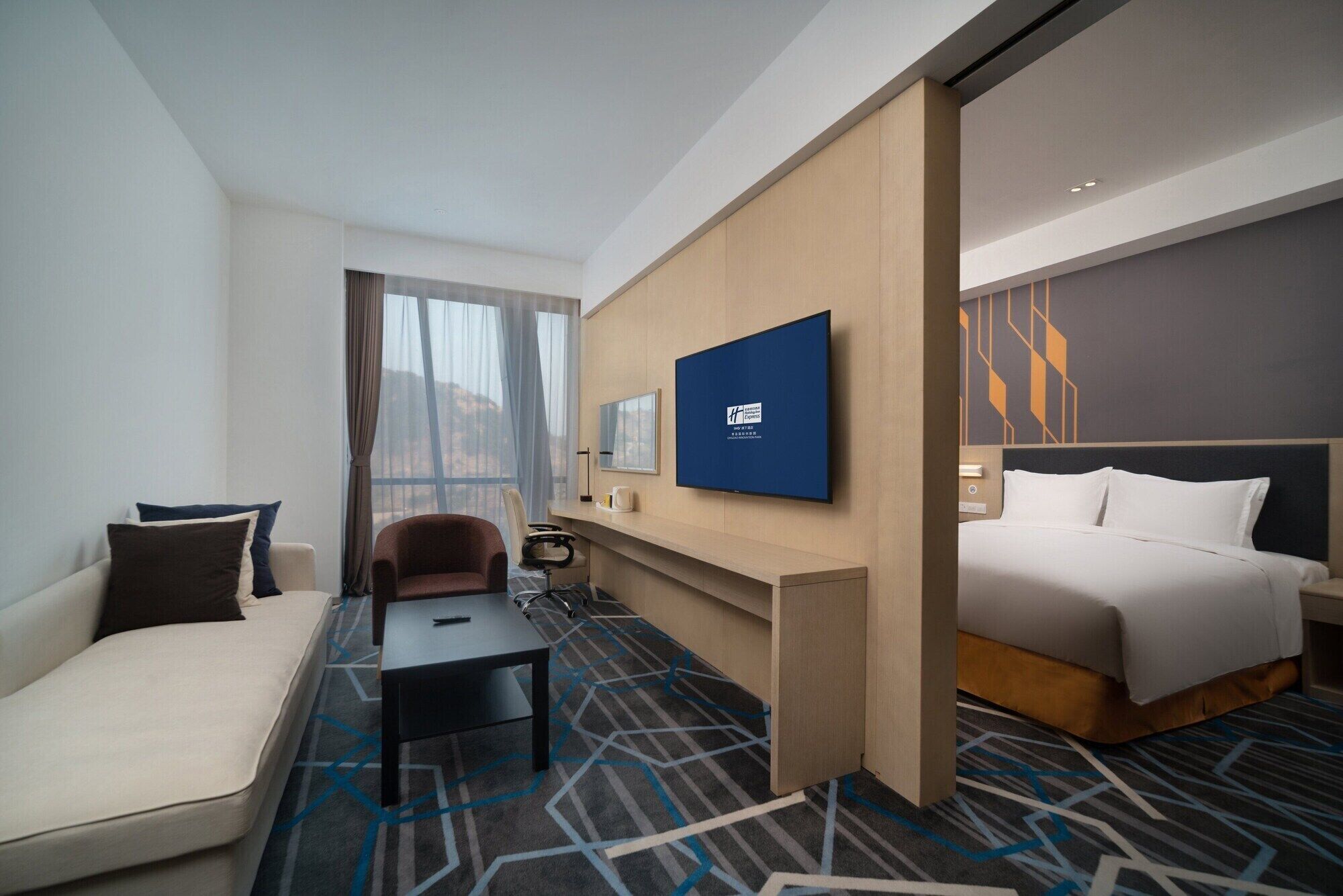 A hotel room with a bed, a sofa, a desk, and a TV mounted on the wall.