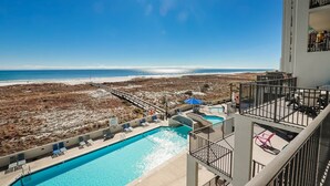 Uma piscina com vista para a praia e oceano, um deck com espreguiçadeiras e uma escadaria que leva a um andar superior.