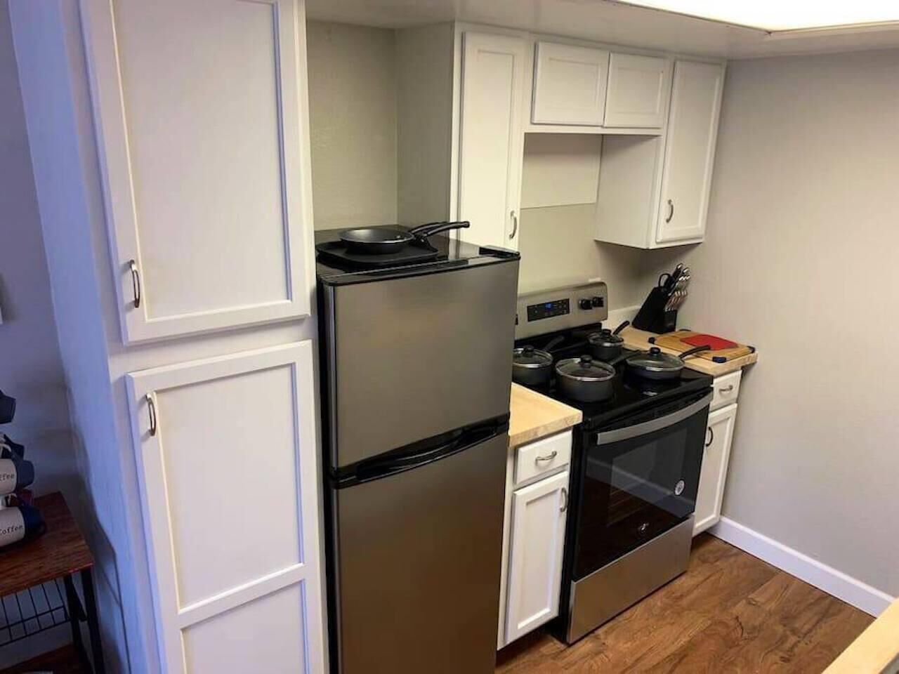 A compact kitchen with white cabinets, a stainless steel refrigerator, a stove, and a dishwasher.
