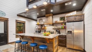 Una cocina con una isla de madera, taburetes de bar, un refrigerador de acero inoxidable y un letrero que dice 'Let's eat'.