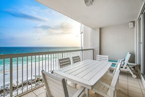 Un balcon avec une table et des chaises blanches, donnant sur une plage et l’océan.
