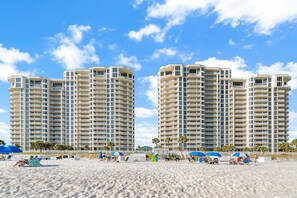 Un hôtel situé en bord de mer, composé de plusieurs immeubles de grande hauteur, doté de parasols et de chaises longues sur la plage.