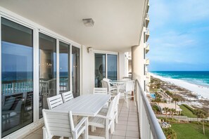 Un balcon avec une table et des chaises, donnant sur une plage et l’océan.