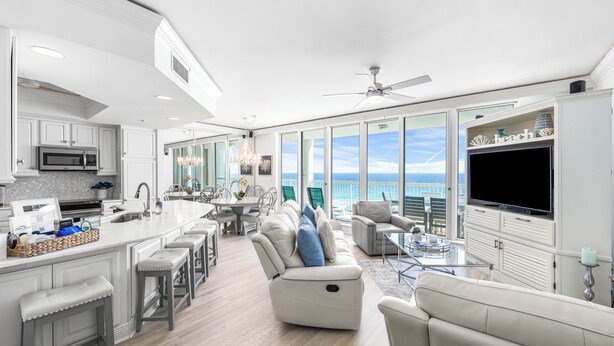 A modern kitchen with a central island, a dining area with a view, and a living room with a large TV and comfortable seating. - 2026 Updated, 5-Star, Modern Beachfront Condo at Silver Beach Towers (Destin)