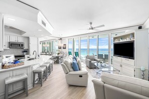Una cocina moderna con una isla central, un comedor con vistas y una sala de estar con televisor grande y asientos cómodos.