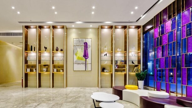 A modern lobby with marble flooring, a central art piece, and a seating area with a colorful glass partition. - Lavande Hotel (Guangzhou)
