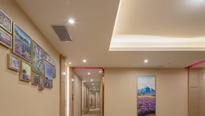 A hotel hallway with framed artwork on the walls, a carpeted floor, and a large painting of a mountain landscape. - Lavande Hotel (Guangzhou)