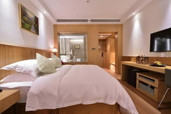 Habitación de hotel con cama, escritorio, televisor y baño visible a través de una puerta de vidrio.