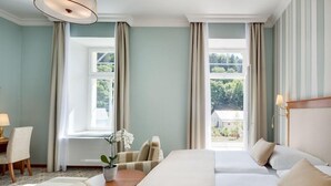 A hotel room with a large bed, two bedside tables, a chair, a small table with a plant, and a view of greenery outside. - Centralni Lazne Ensana Health Spa Hotel (Marianske Lazne)