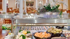 A buffet area with various food items, including seafood, fruits, and cheeses, in a well-lit dining hall with wooden chairs and a large floral centerpiece. - Centralni Lazne Ensana Health Spa Hotel (Marianske Lazne)
