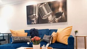Un salon avec un canapé bleu, une table basse blanche et un plateau sur lequel se trouvent un vase et des bouteilles.