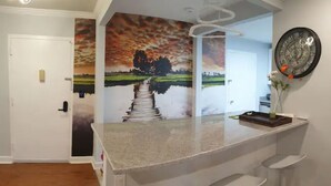 Une cuisine avec un coin bar, une porte blanche et un mur orné d’un tableau représentant un coucher de soleil.