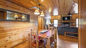 Interno di una baita in legno con zona pranzo, soggiorno con camino e televisione.