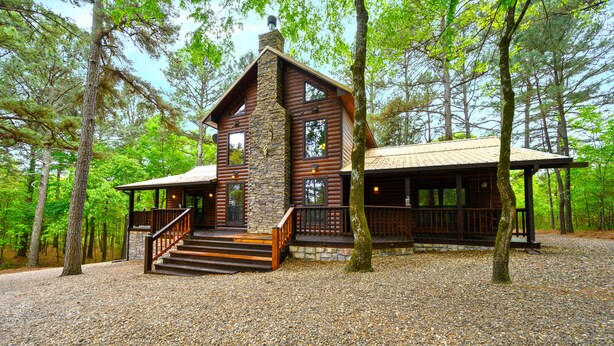 Una baita di legno con camino in pietra, veranda in legno e vialetto sterrato.