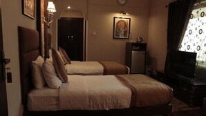 Une chambre d’hôtel avec deux lits, un bureau, une télévision et une horloge au mur.