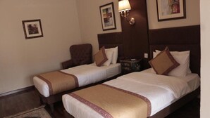 Une chambre d’hôtel avec deux lits simples, un petit fauteuil, une table de chevet et un tapis décoratif.