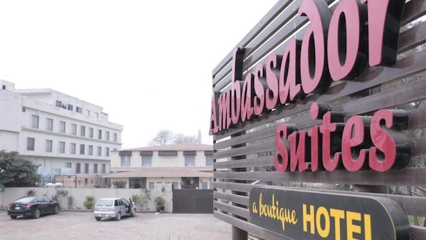Une enseigne pour l’hôtel Ambassador Suites, un hôtel de charme, avec un bâtiment moderne en arrière-plan.