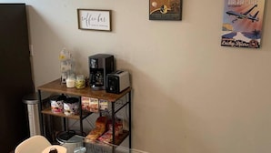 A kitchenette with a coffee maker, toaster, and various food items on a shelf. There are two framed pictures on the wall. - "Air Commando-Condo" Perfect Location in Clovis, NM (Clovis)