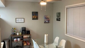 A compact kitchen with a glass dining table, white chairs, a ceiling fan, and a window with blinds. - "Air Commando-Condo" Perfect Location in Clovis, NM (Clovis)