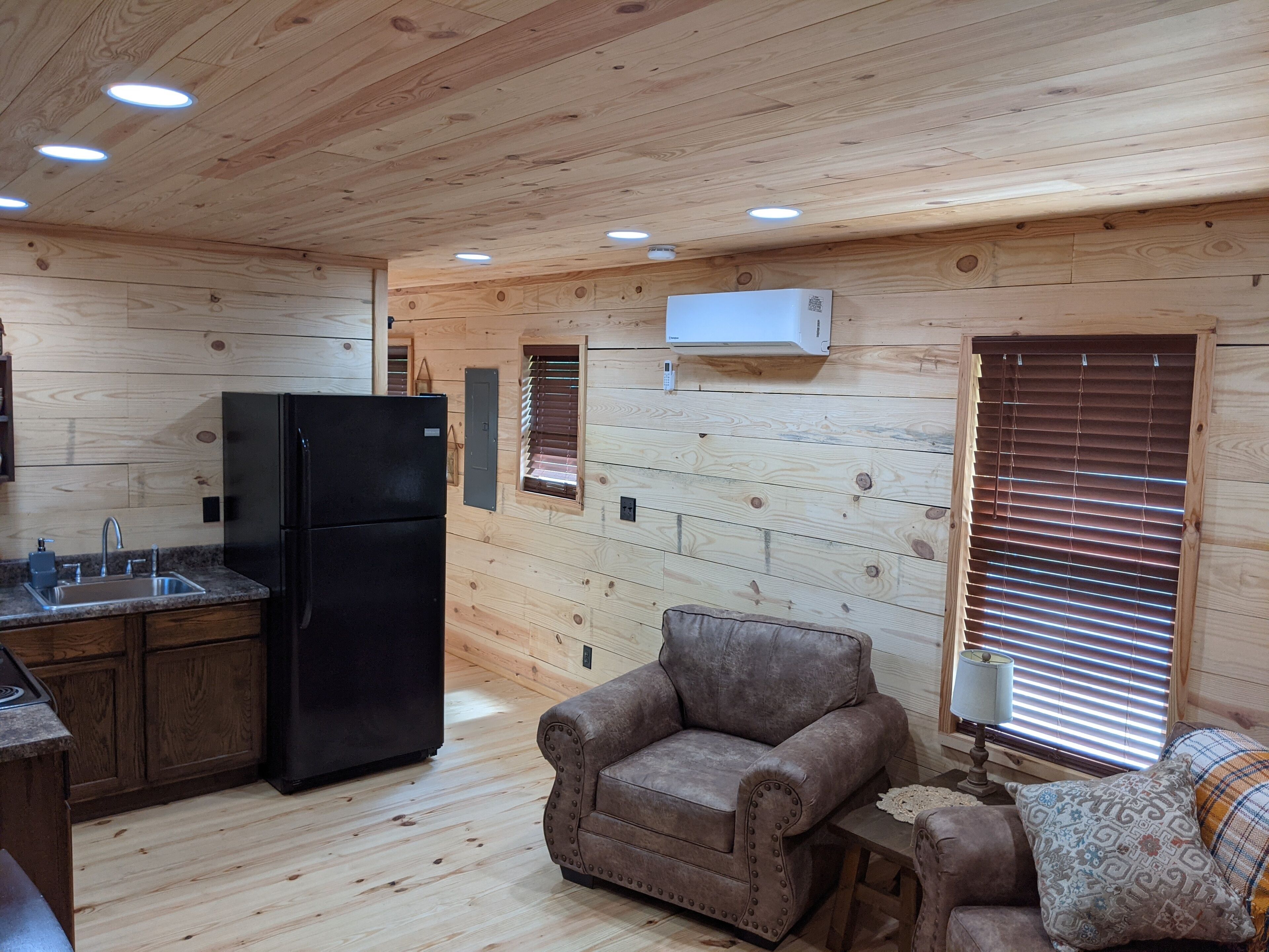A cozy cabin-style room with a kitchenette, a sofa, and a window with blinds.