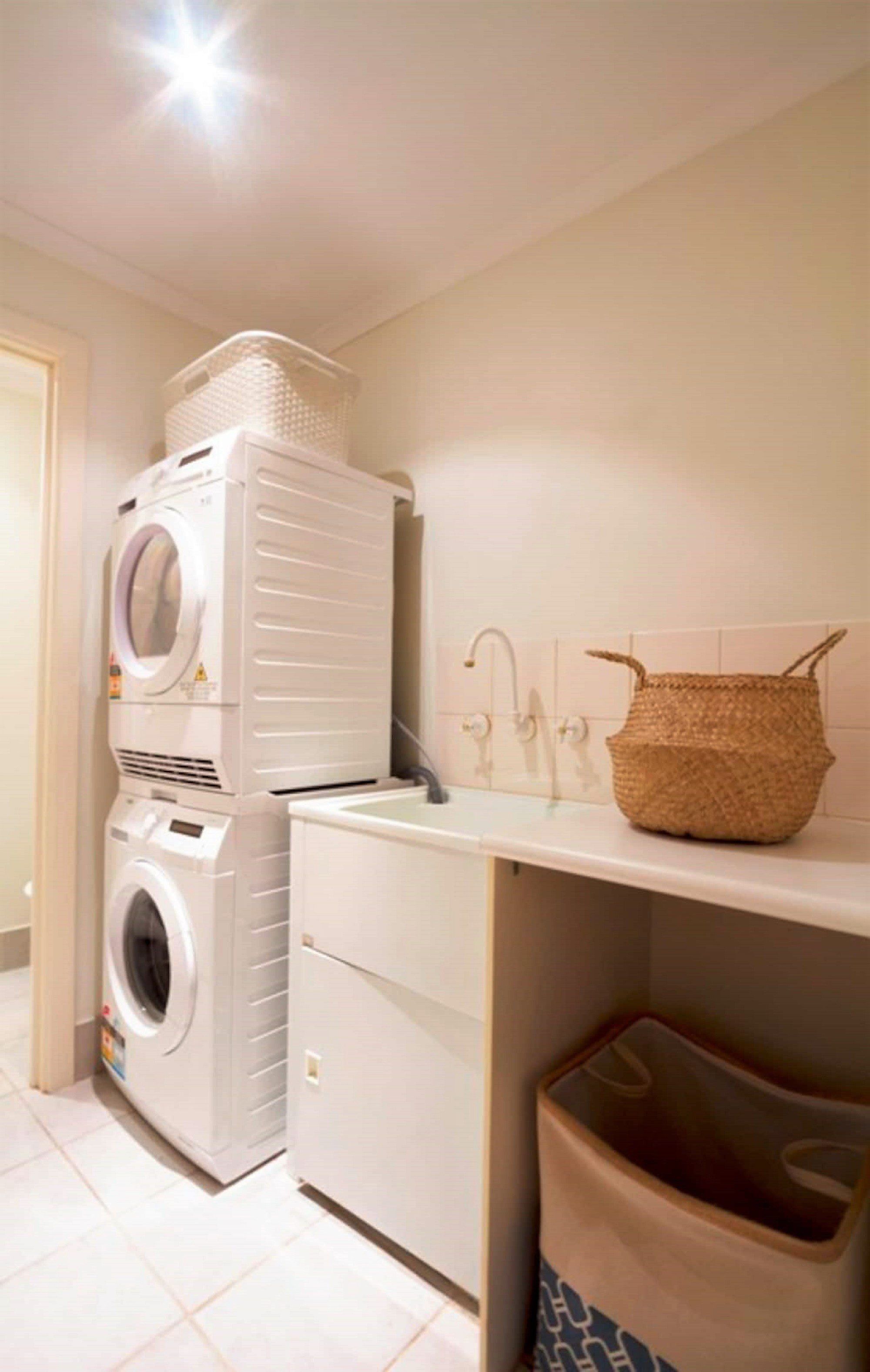 A laundry area with stacked washing machines and a basket on a shelf.