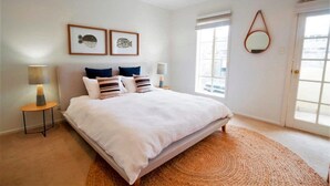 A bedroom with a large bed, two bedside tables with lamps, a round mirror on the wall, and two framed pictures above the bed. - Adelaide | 3BR Norwood Townhouse | Fringe Stay + Wi-Fi + Parking + Smart TV | Walk Everywhere (Norwood)