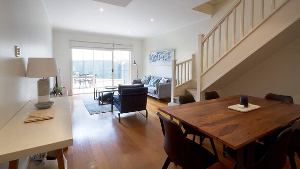 A spacious living area with a wooden dining table, a sofa, and a staircase. - Adelaide | 3BR Norwood Townhouse | Fringe Stay + Wi-Fi + Parking + Smart TV | Walk Everywhere (Norwood)
