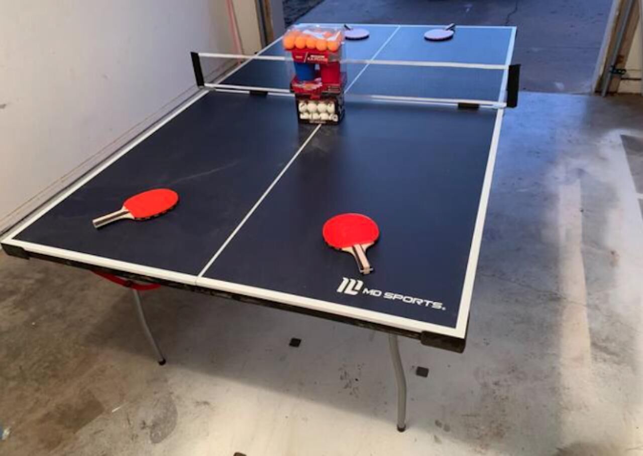 Een tafeltennistafel met twee rode batjes en een stapel oranje tafeltennisballen.