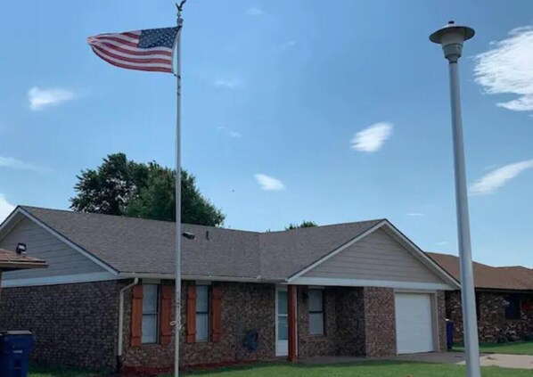 A two-story building with a brick facade, a garage, and an American flag. - Convenient to Wind Farms, Wedding Venue, Hunting, Large Yard-Pet Friendly! (Lahoma)