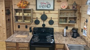 A kitchen with wooden walls, a stove, and shelves with dishes and cookware.