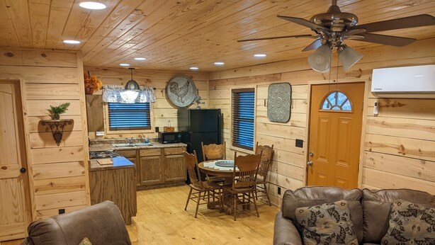 A cozy cabin interior with wooden walls, a dining area, a kitchen, and two leather sofas.
