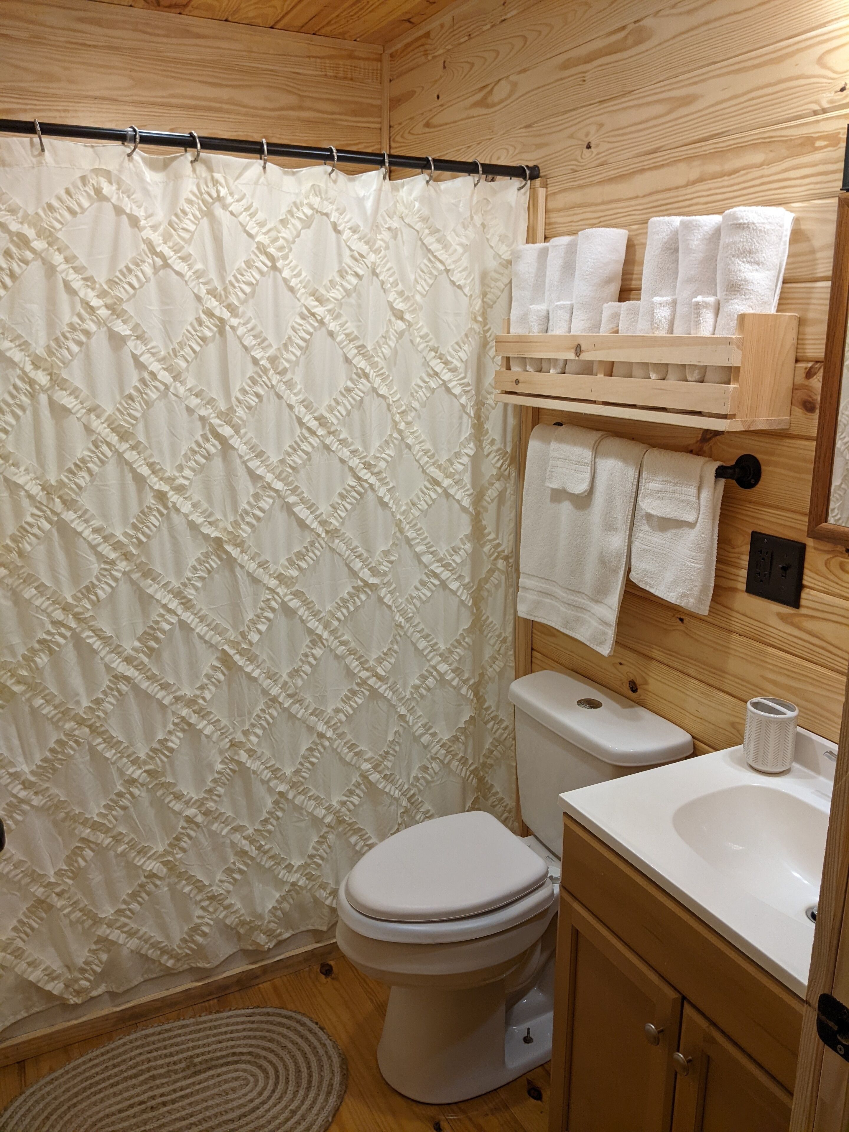A wooden bathroom with a toilet, sink, and a shower curtain.
