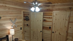 A wooden room with a bed, a desk, a lamp, and a ceiling fan.