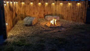A backyard with a wooden fence, a fire pit, and string lights.