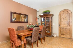 Une salle à manger avec une table en bois, des chaises en osier, un buffet aux portes vitrées et une porte en bois.