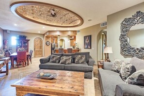A spacious living room with a large round ceiling fan, a dining area with a wooden table, and a kitchen in the background.