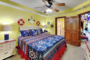 A bedroom with a bed, nightstands, a ceiling fan, and nautical-themed decor.