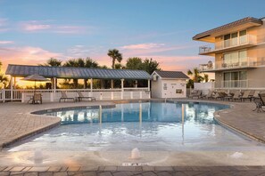 A swimming pool with a covered area, lounge chairs, and a building with balconies. - Pet friendly condo w. community pool + partial ocean views! (Tybee Island)