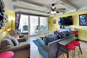 Una sala de estar con sofá, sillones, televisor y un balcón con mobiliario exterior.