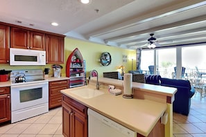 A kitchen with wooden cabinets, a microwave, an oven, a dishwasher, a sink, and a dining area with a ceiling fan. - Pet friendly condo w. community pool + partial ocean views! (Tybee Island)